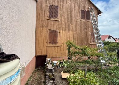 Façade en bardage bois presque totalement recouverte par une nouvelle couche de lasure protectrice.
