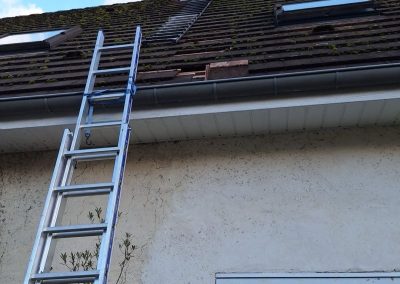 Artisan ramoneur sécurisé sur un toit en pente, intervenant sur un conduit de cheminée en inox via une échelle de toit.